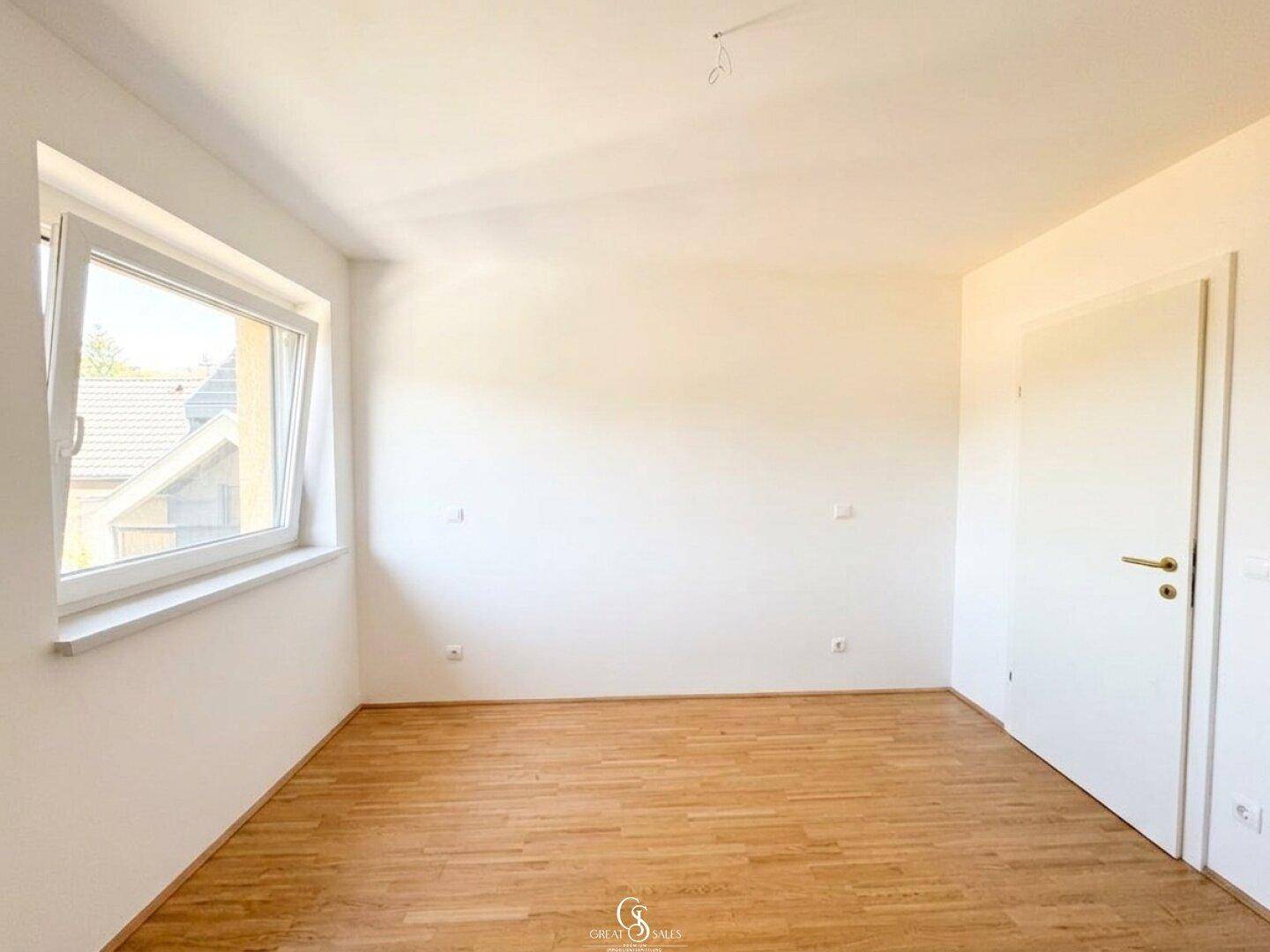 Helles Schlafzimmer mit Holzboden und einem Fenster, das viel Tageslicht hereinlässt und eine angenehme Atmosphäre schafft.