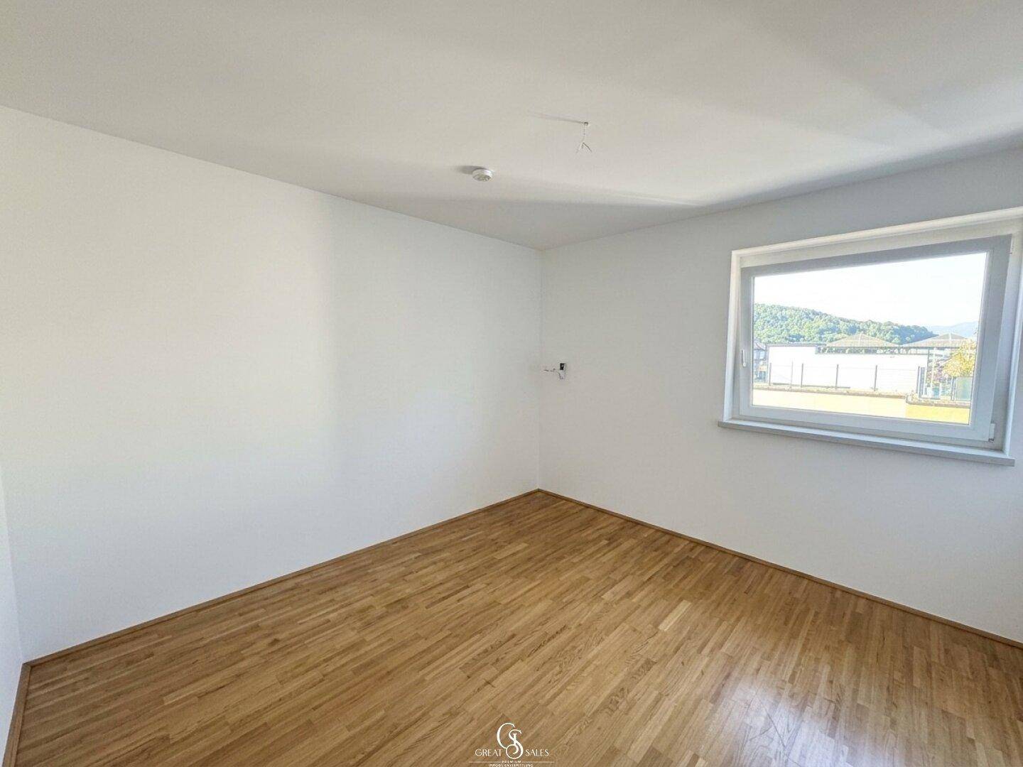 Geräumiges Schlafzimmer mit Holzboden und einem Fenster, das viel Tageslicht hereinlässt und eine offene Sicht bietet.