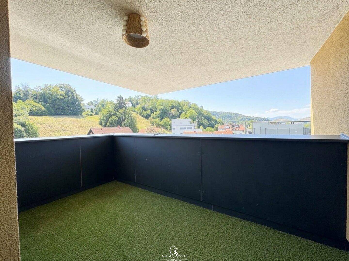 Geräumiger Balkon mit Kunstrasen und weitem Blick über die grüne Umgebung und die Dächer der Stadt.