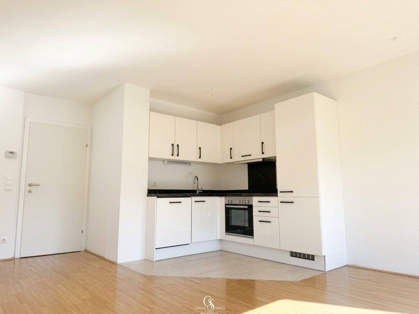 Moderne Einbauküche mit weißen Hochglanzschränken, schwarzer Arbeitsplatte und integriertem Backofen.