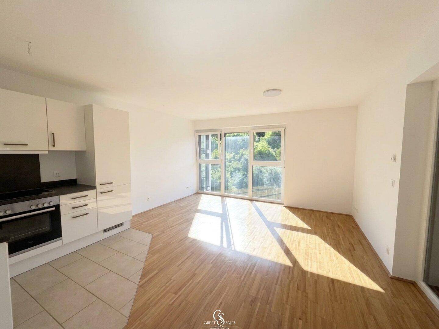 Offener Wohnbereich mit integrierter Küchenzeile, Holzboden und Zugang zum sonnigen Balkon.