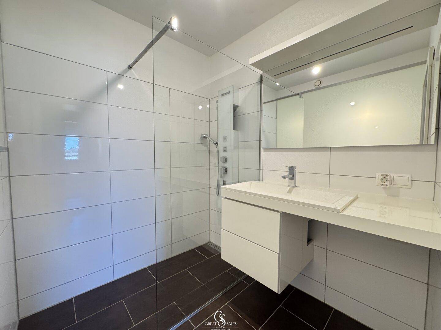 Modernes Badezimmer mit großer begehbarer Dusche, weißen Fliesen und einem stilvollen Waschtisch mit Spiegel.