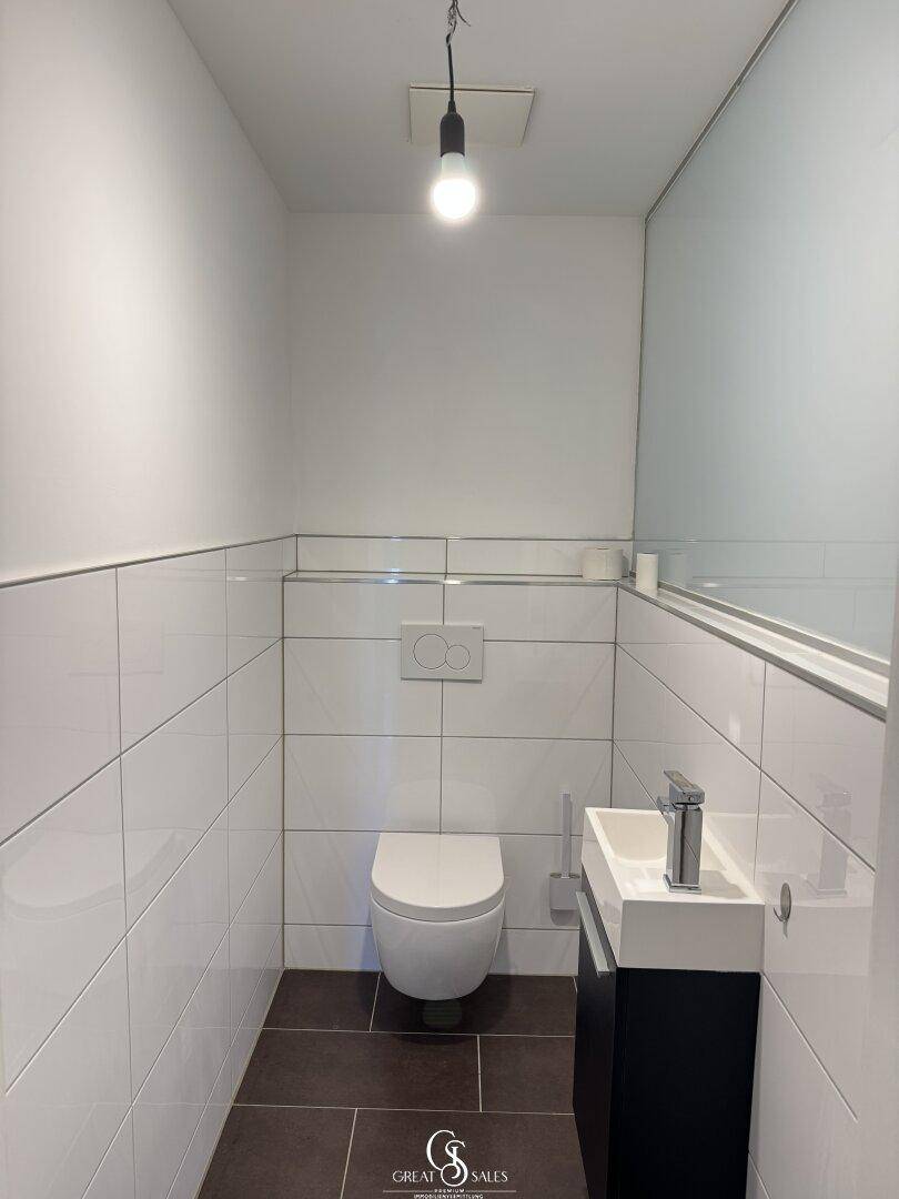 Separates Gäste-WC mit wandhängender Toilette, kleinem Waschbecken und modernen, halbhoch gefliesten Wänden.