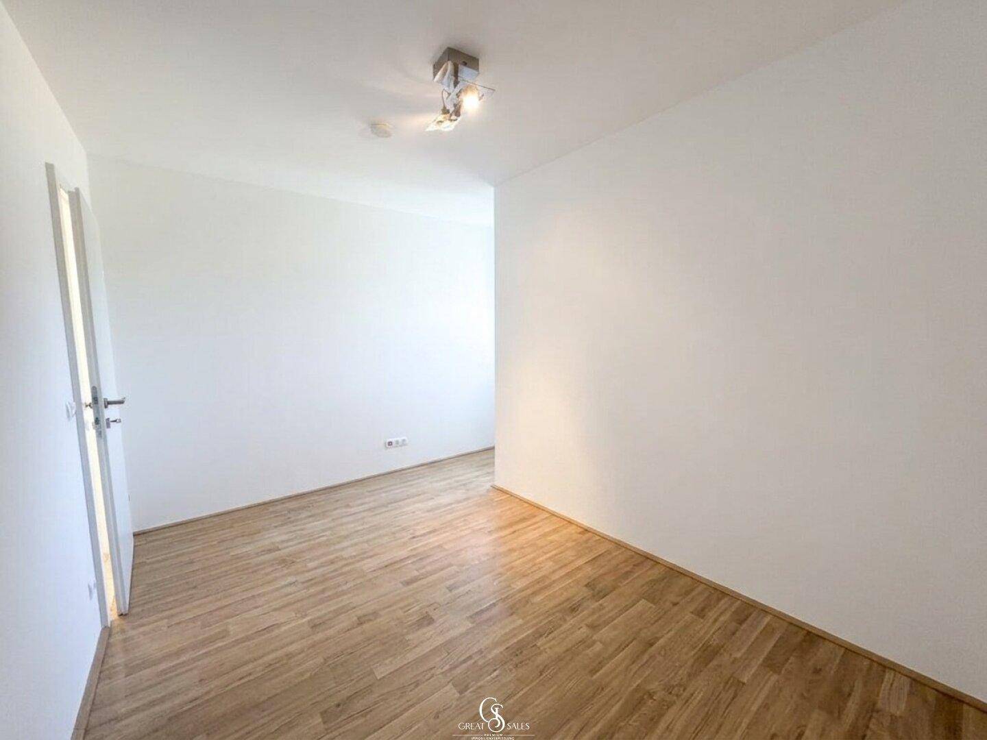 Helles Zimmer mit Holzboden und einer Tür, ideal als Schlaf- oder Arbeitszimmer nutzbar.