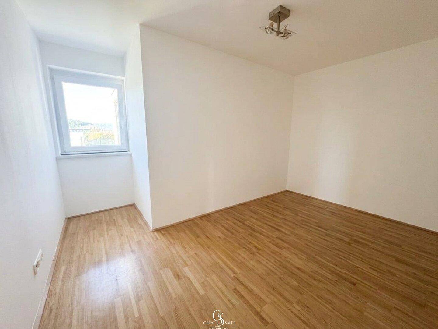 Helles Schlafzimmer mit Holzboden und einem Fenster, das einen angenehmen Blick ins Grüne bietet.