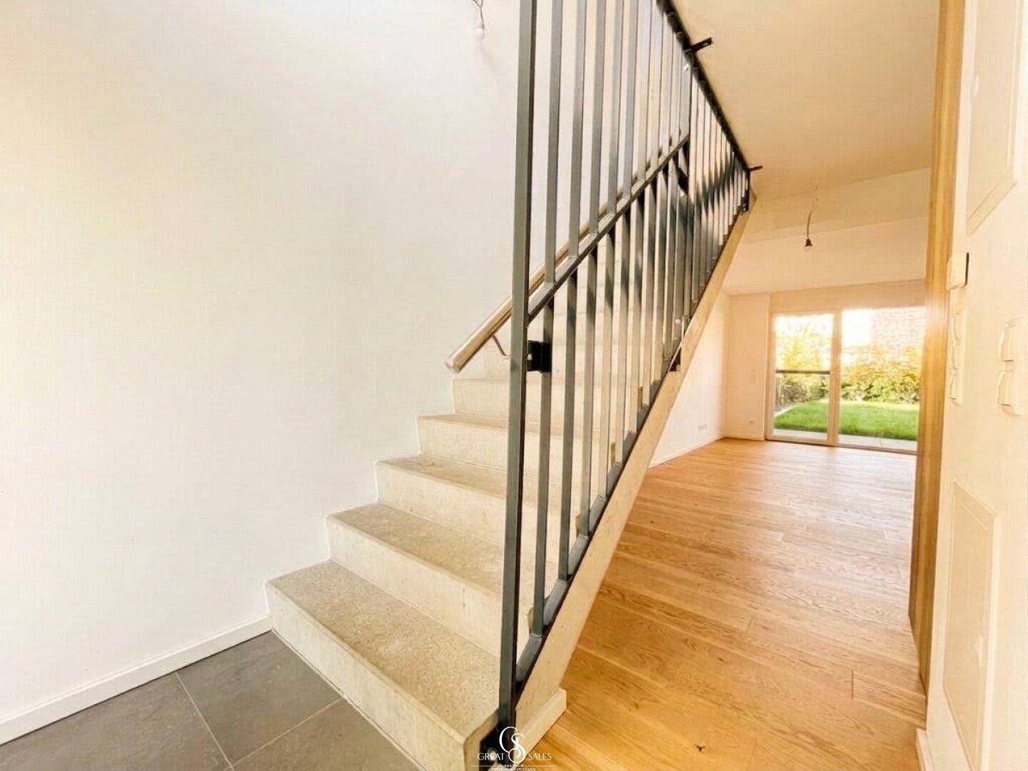 Moderner Eingangsbereich mit heller Treppe und Holzfußboden, der zum Garten führt.