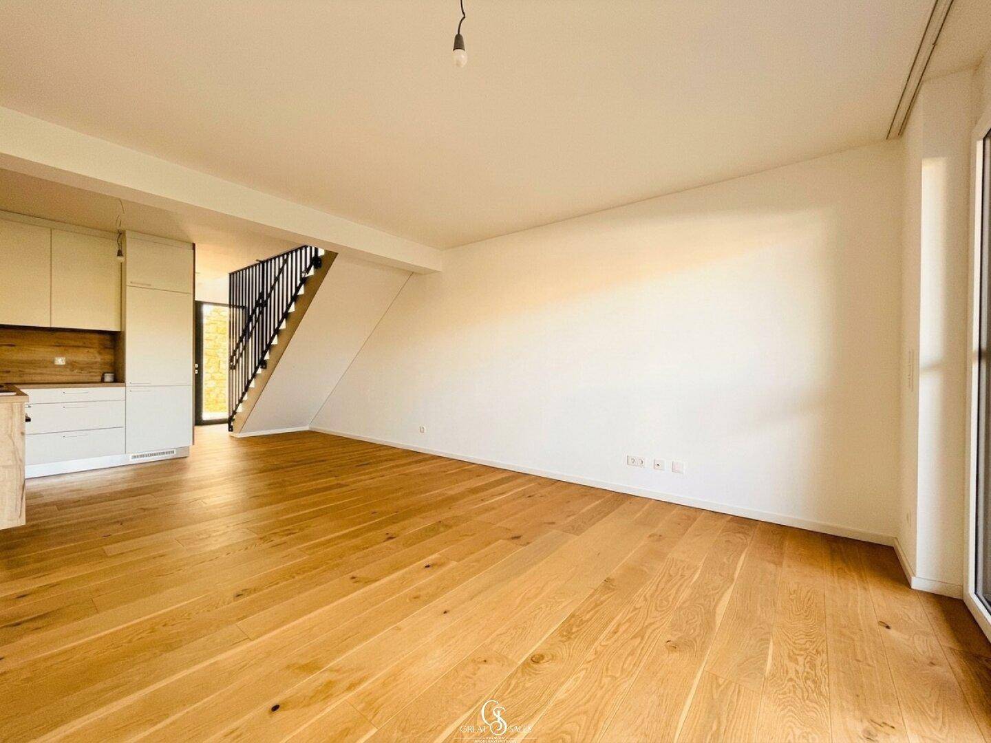 Heller Wohnbereich mit offener Küche und Treppenzugang, ausgestattet mit modernem Holzfußboden.