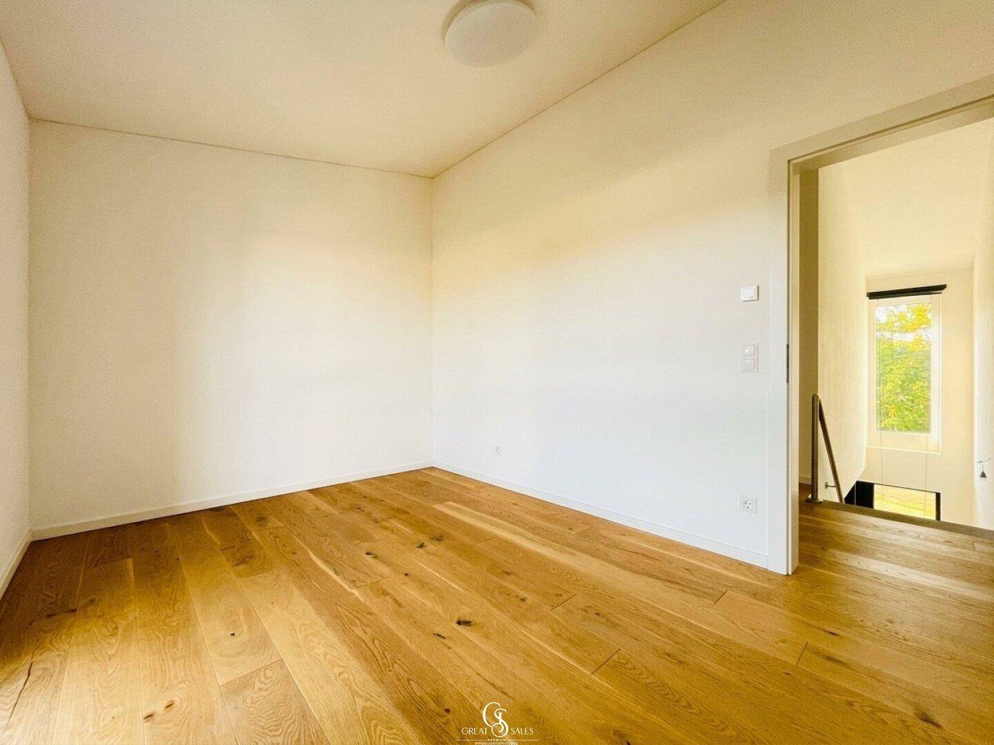 Geräumiges Zimmer mit hellem Holzboden und Zugang zum Treppenhaus, ideal als Schlafzimmer.