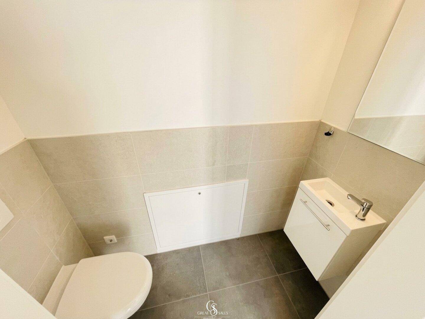 Modernes Gäste-WC mit Wand-WC, kleinem Waschbecken und hellen Fliesen.