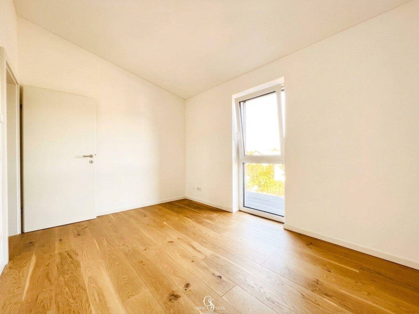 Helles Schlafzimmer mit Holzboden und großem Fenster, das viel Tageslicht hereinlässt.