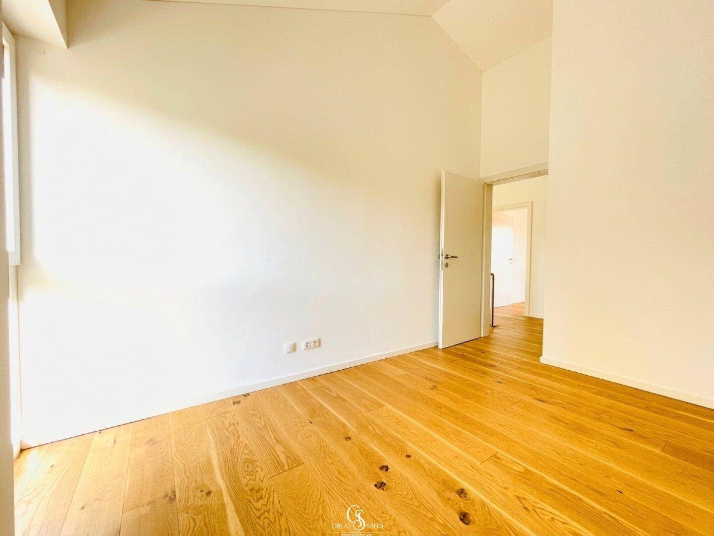 Lichtdurchflutetes Zimmer mit Holzboden und weiß gestrichenen Wänden, bereit zur individuellen Gestaltung.