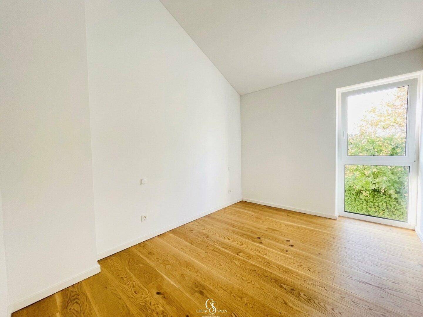 Helles Zimmer im Dachgeschoss mit schräger Decke, Holzboden und großem Fenster.