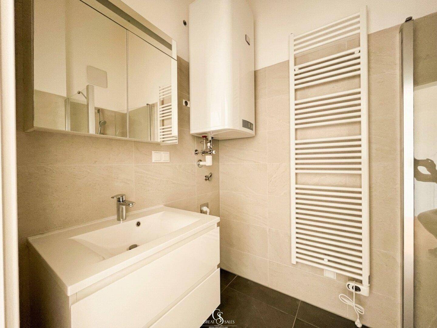 Modernes Badezimmer mit Waschbecken, Spiegelschrank, Handtuchheizkörper und Boiler.