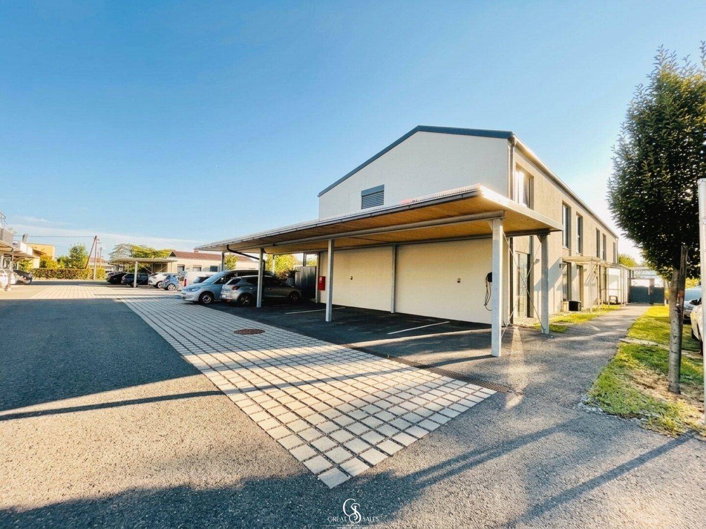 Außenansicht der Reihenhäuser mit Carports und Parkplätzen unter blauem Himmel.