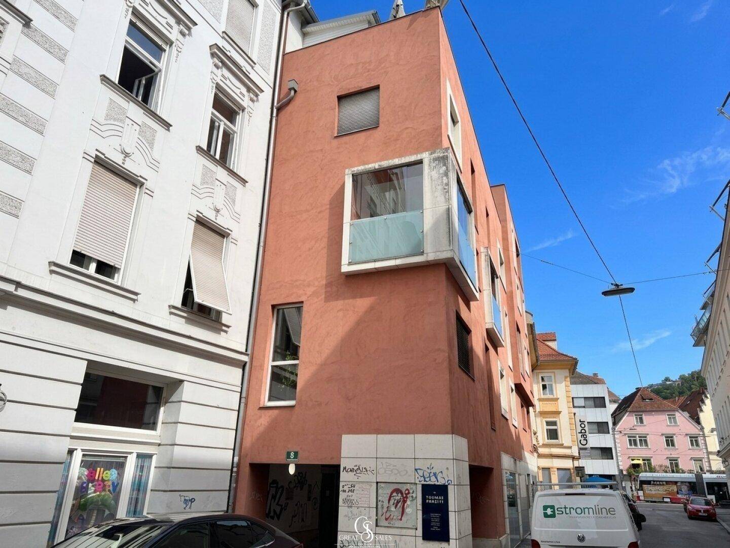 Moderne Fassade eines Gebäudes in der Stadt mit markanten Erkerfenstern und einer lebhaften orangefarbenen Putzfassade, umgeben von älteren Bauten.