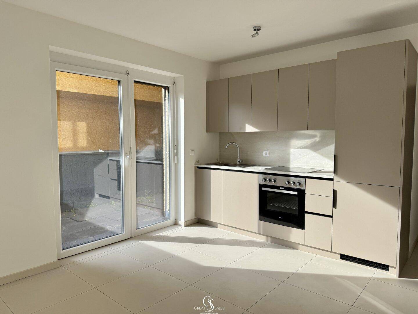 Moderne Einbauküche in Beige mit Ofen, Spüle und direktem Zugang zu einer Terrasse.