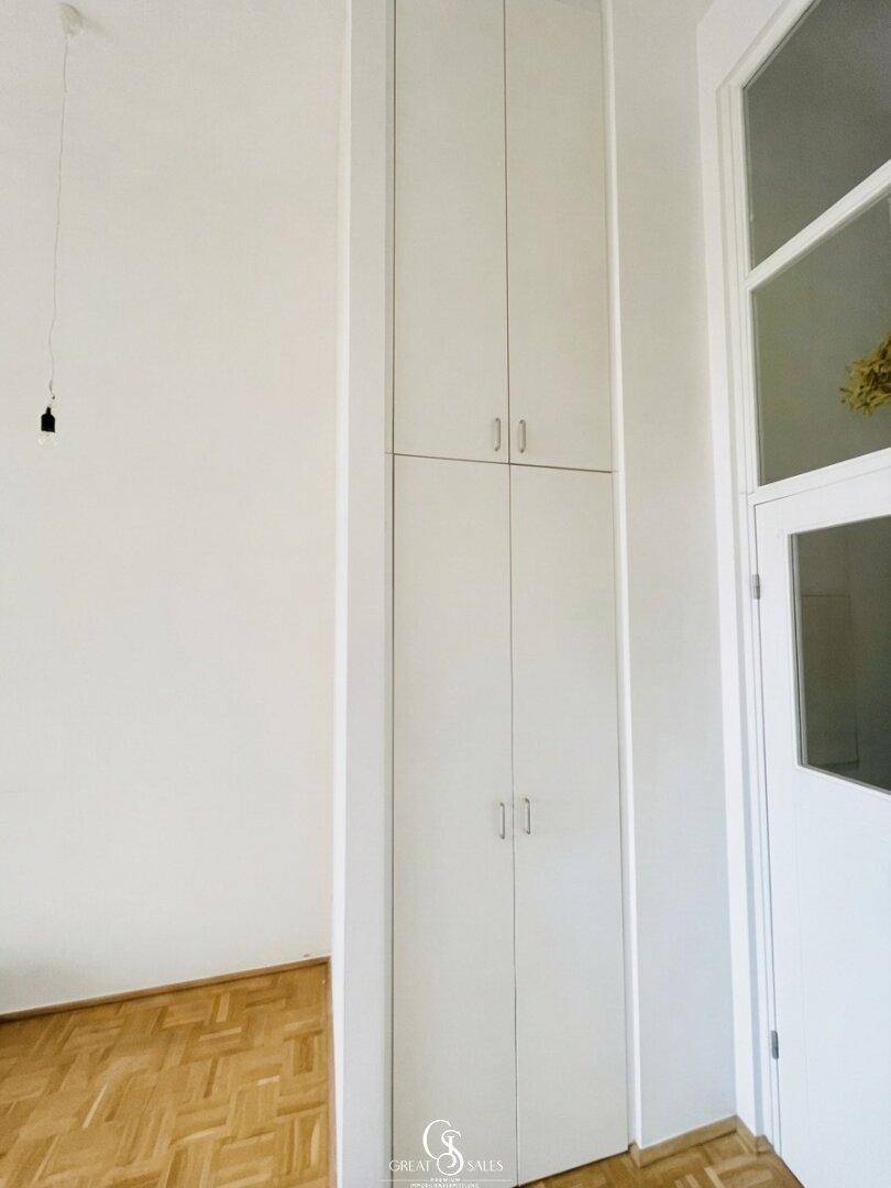Hoher weißer Einbauschrank im Flur mit Parkettboden und Tür mit Glaseinsätzen.