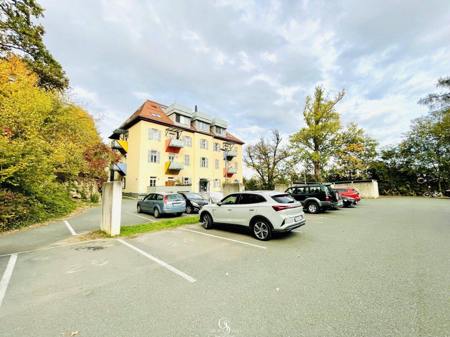 Mehrstöckiges Gebäude mit gelber Fassade und Parkplätzen umgeben von Herbstbäumen.
