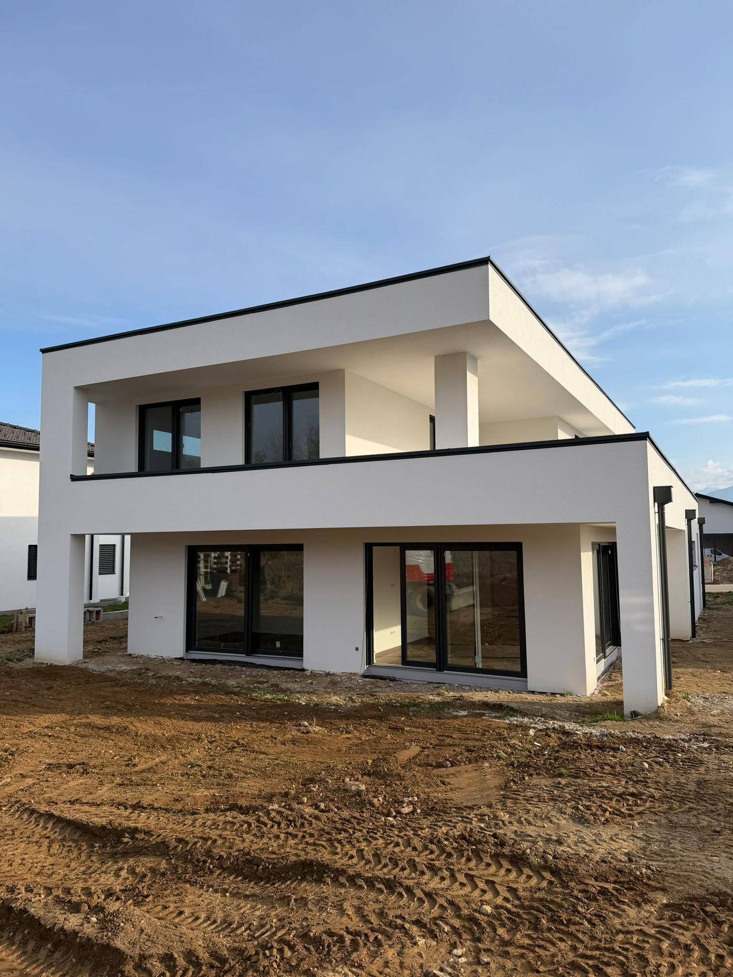 Modernes Neubau-Einfamilienhaus mit klarer Architektur, weißer Fassade, großen Glasfronten und einem Balkon im Obergeschoss.