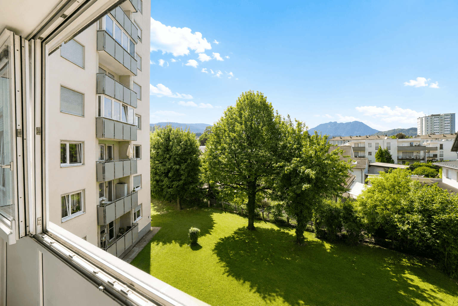Ausblick auf eine grüne Gartenanlage und umliegende Wohngebäude an einem sonnigen Tag mit blauem Himmel.