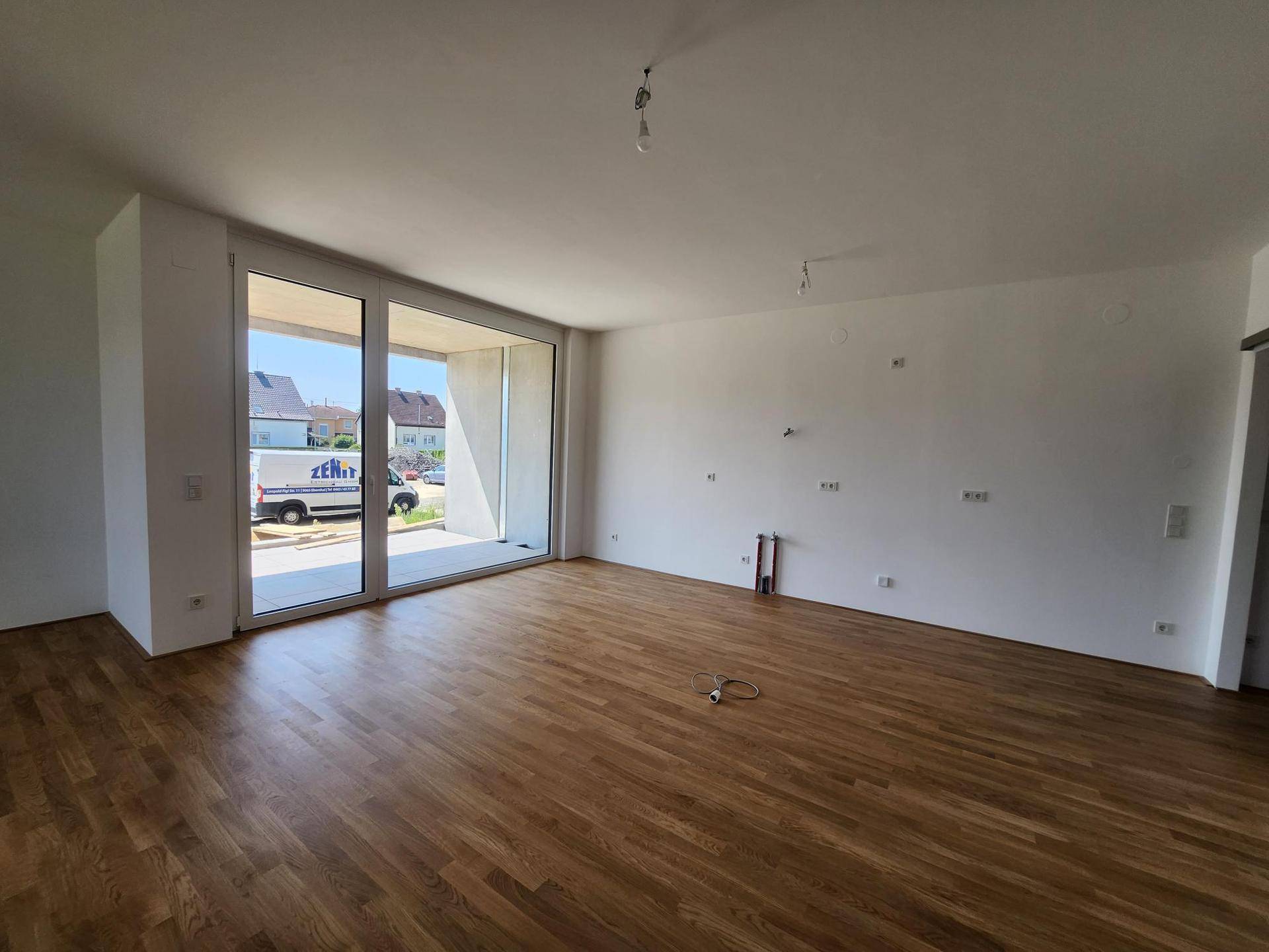 Heller Wohnbereich mit Holzboden und großer Fensterfront zum Außenbereich.