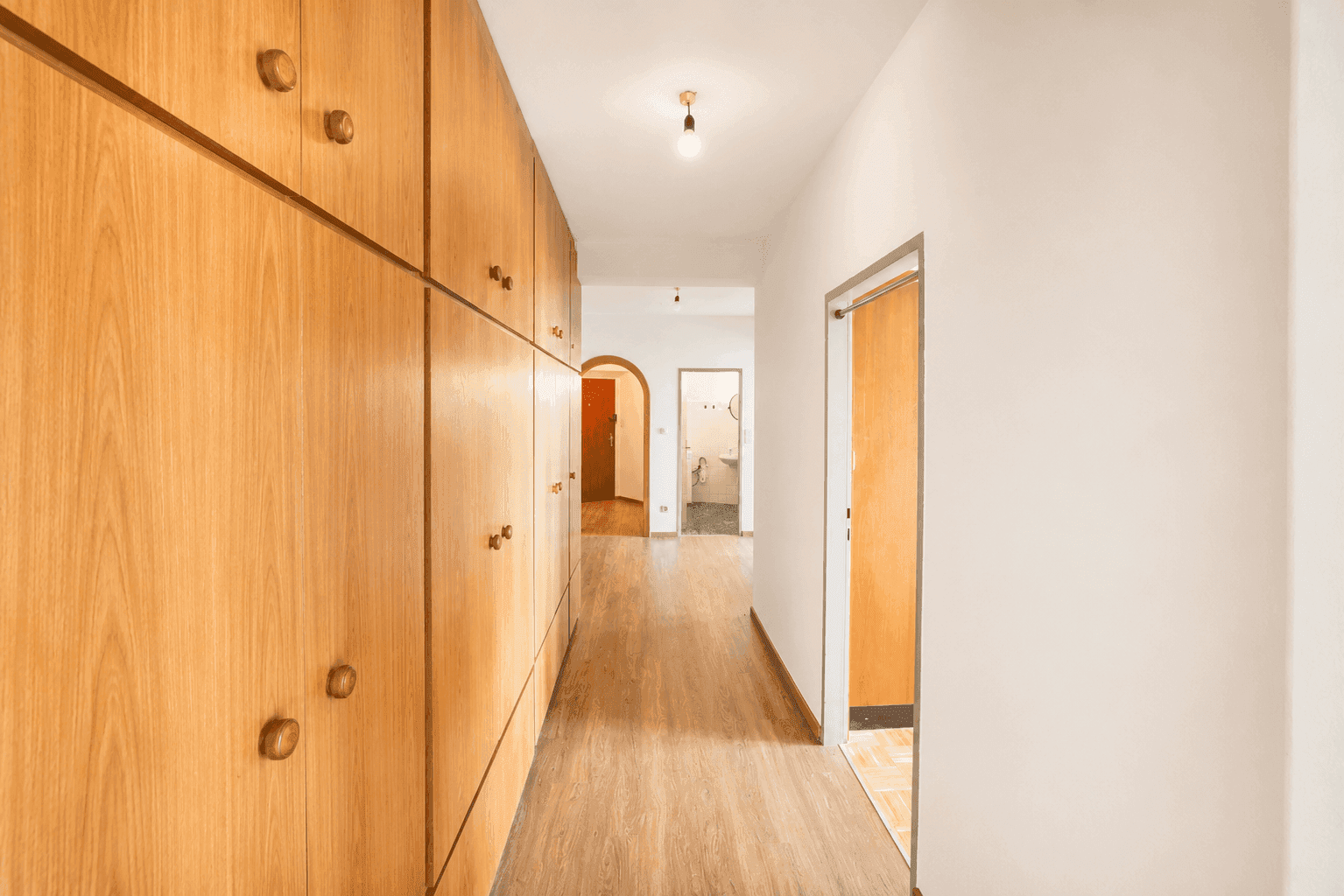 Heller Flur mit praktischen Einbauschränken aus Holz und Laminatboden, der zu weiteren Räumen führt.