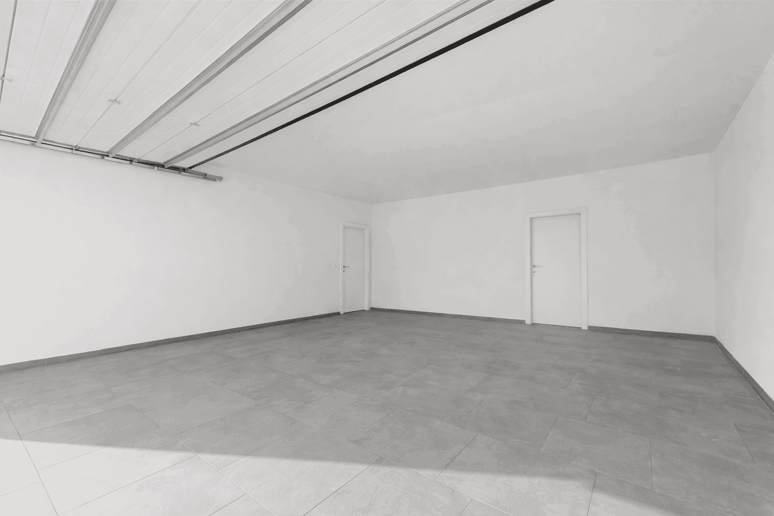 Geräumige Garage mit Fliesenboden und weißen Wänden, ideal für Fahrzeuge und Lagerung.