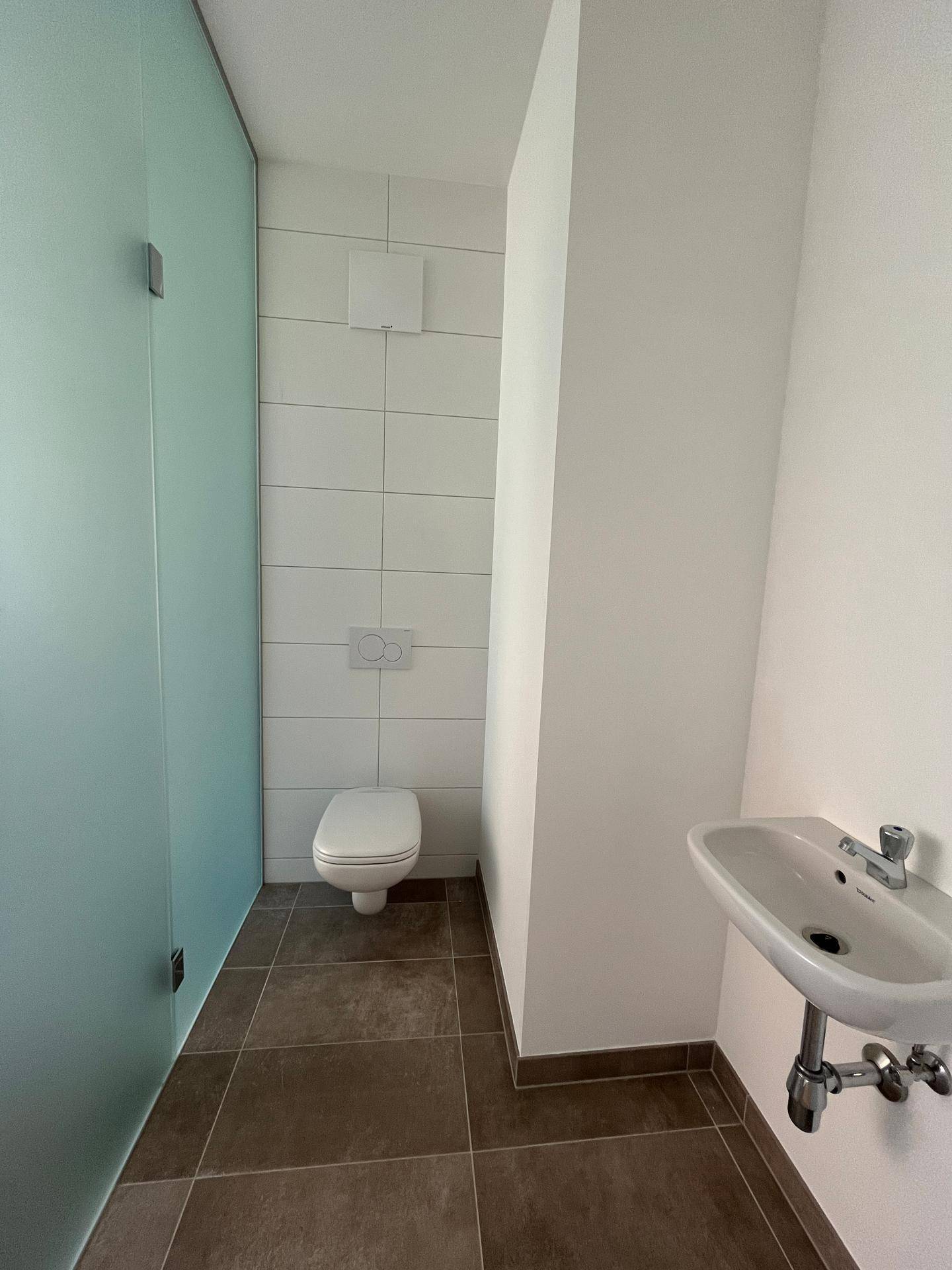 Separates WC mit wandhängender Toilette und kleinem Waschbecken, modern gefliest.