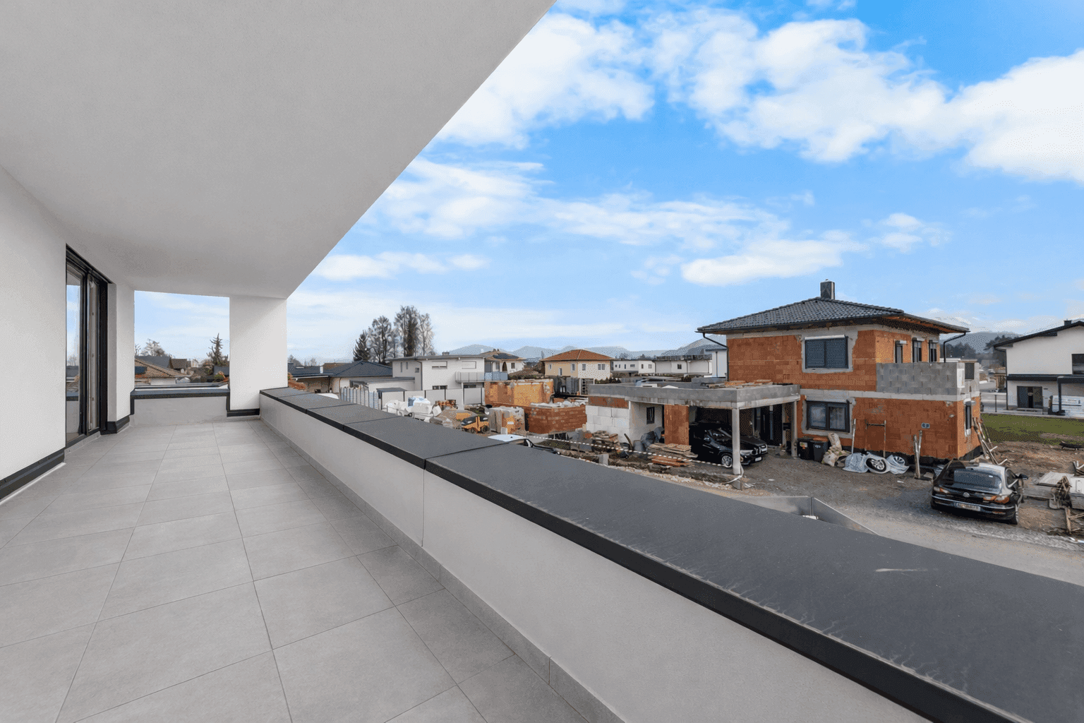Weitläufiger Balkon mit Fliesenboden und Blick auf die umliegende Wohnbebauung und Baustellen.