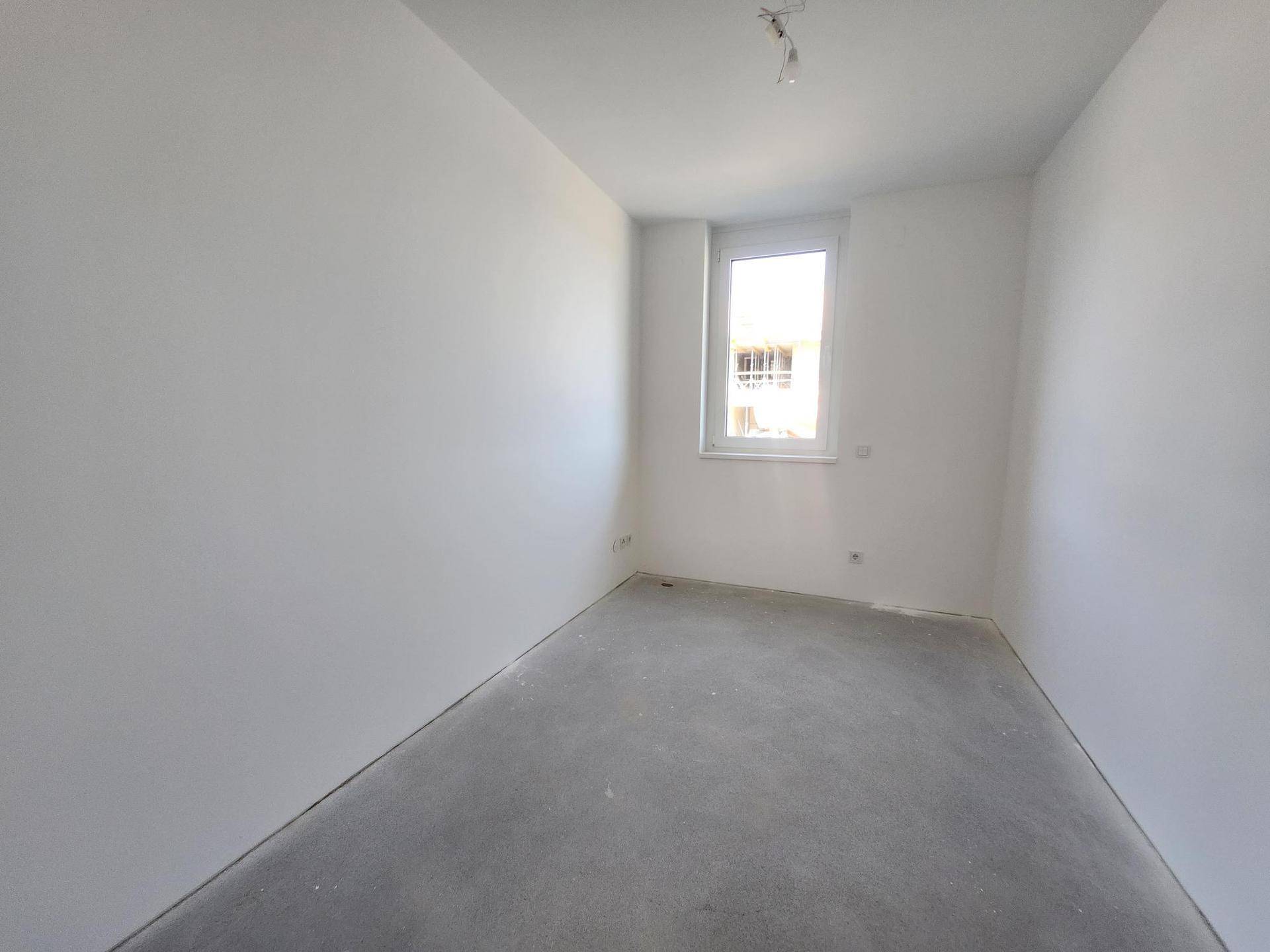 Heller, unmöblierter Raum mit Betonboden und einem Fenster, bereit für den Ausbau.