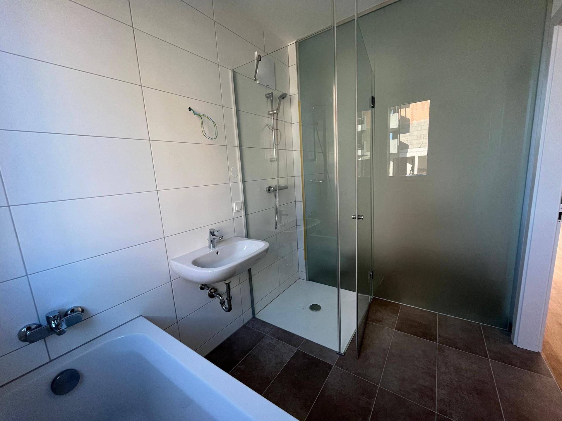 Modernes Badezimmer mit Duschkabine aus Glas und einem schlichten Waschbecken.