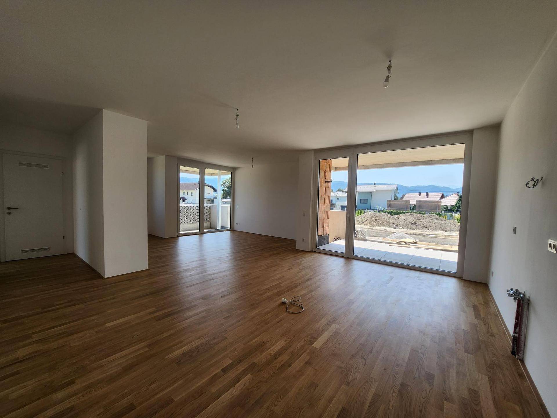 Geräumiger Wohnbereich mit Holzboden und Zugang zu einem Balkon mit Blick auf die Umgebung.