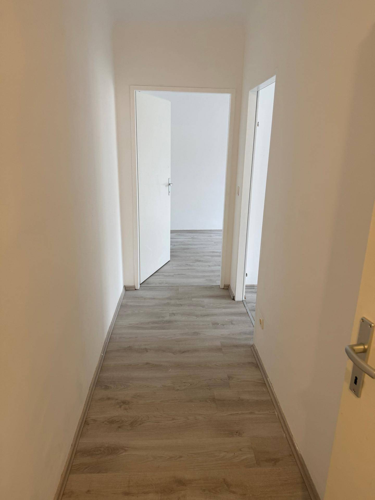 Langer, heller Flur mit Laminatboden, der zu weiteren Zimmern führt.