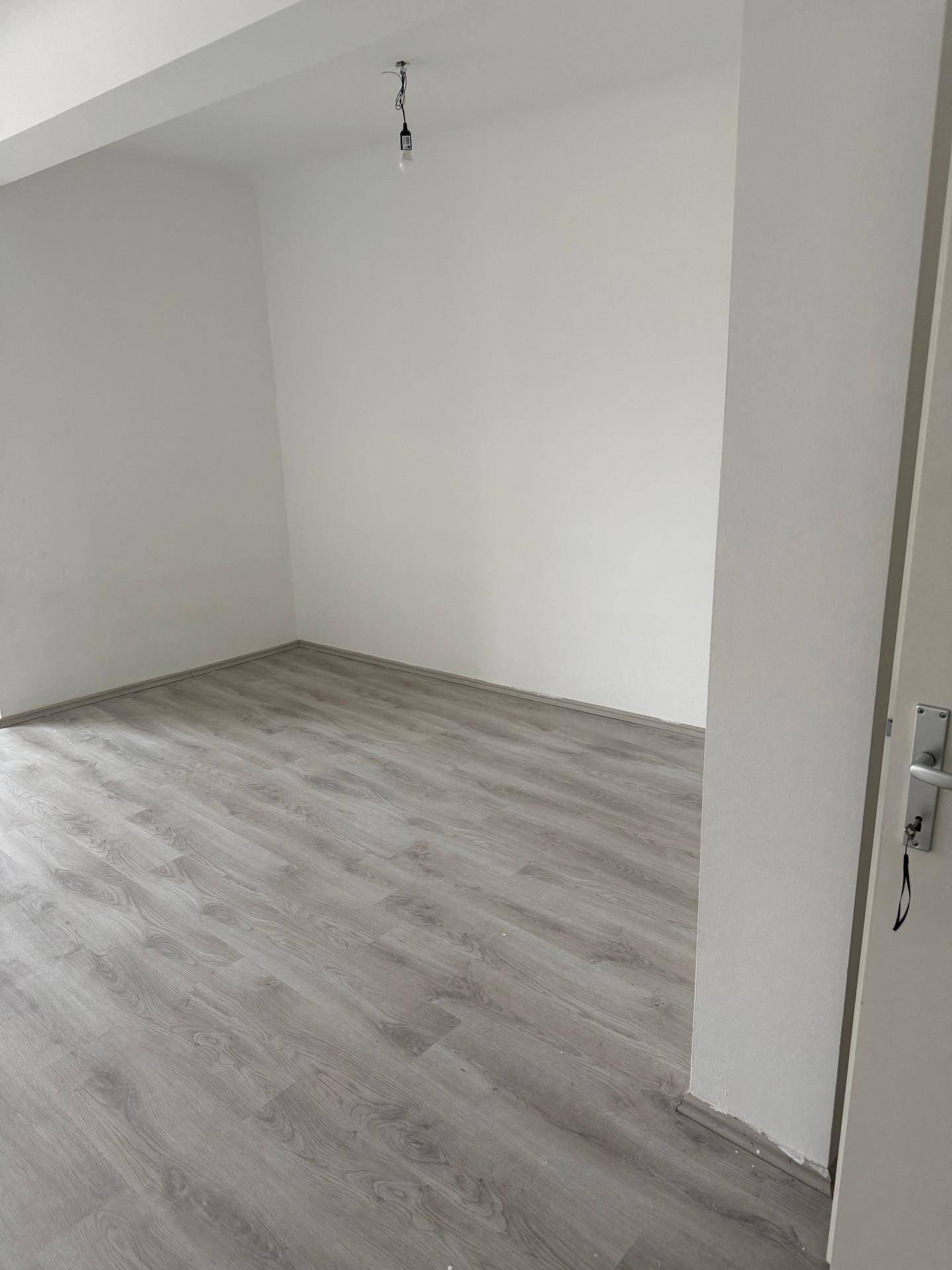 Geräumiger, heller Wohnbereich mit Laminatboden und weiß gestrichenen Wänden.