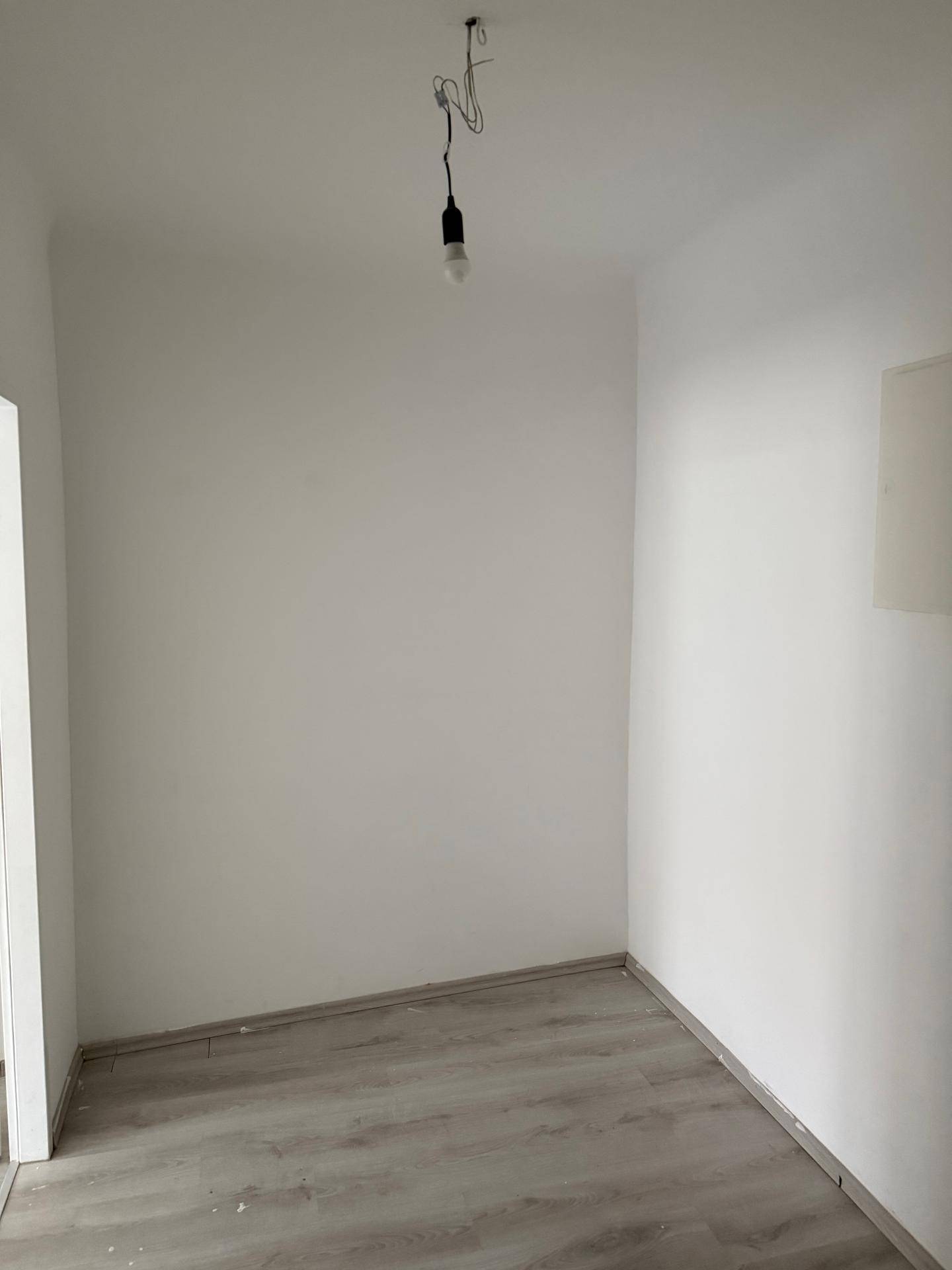 Kleiner, leerer Raum mit weiß gestrichenen Wänden und Laminatboden.