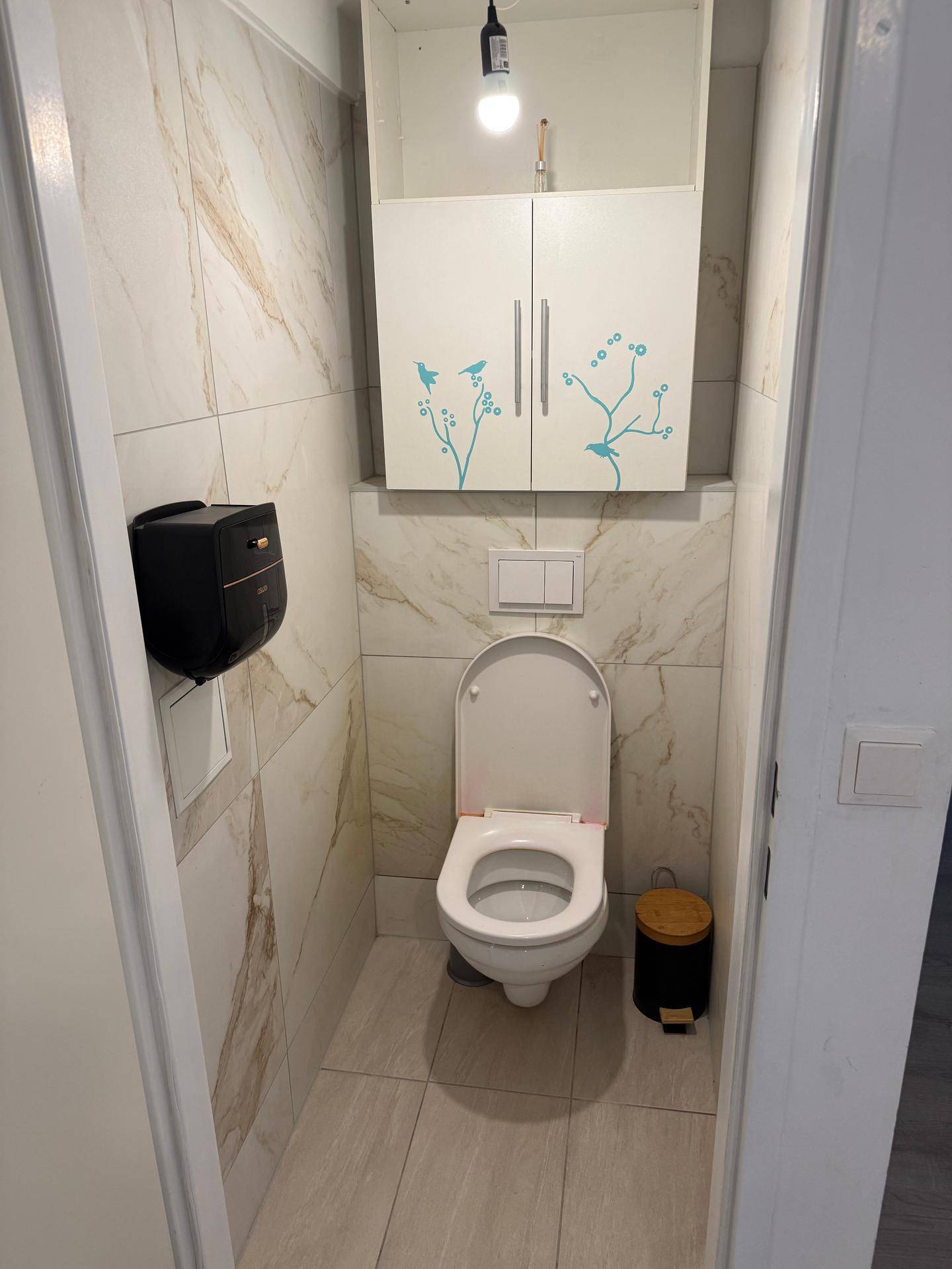 Modern gefliestes Gäste-WC mit Wand-WC und einem kleinen Hängeschrank.