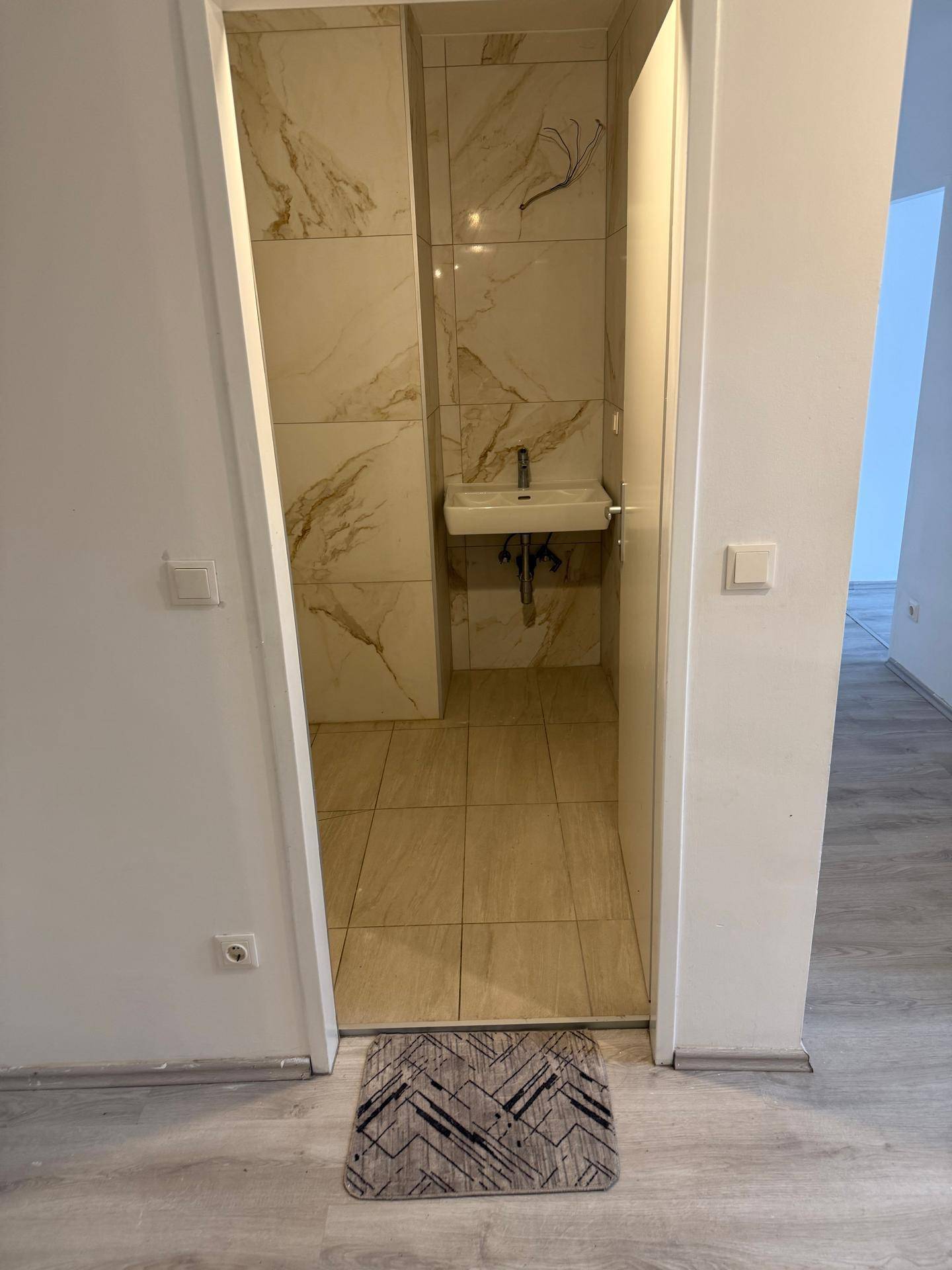 Kleines Badezimmer mit beigefarbenen Fliesen und einem Waschbecken, gut beleuchtet.