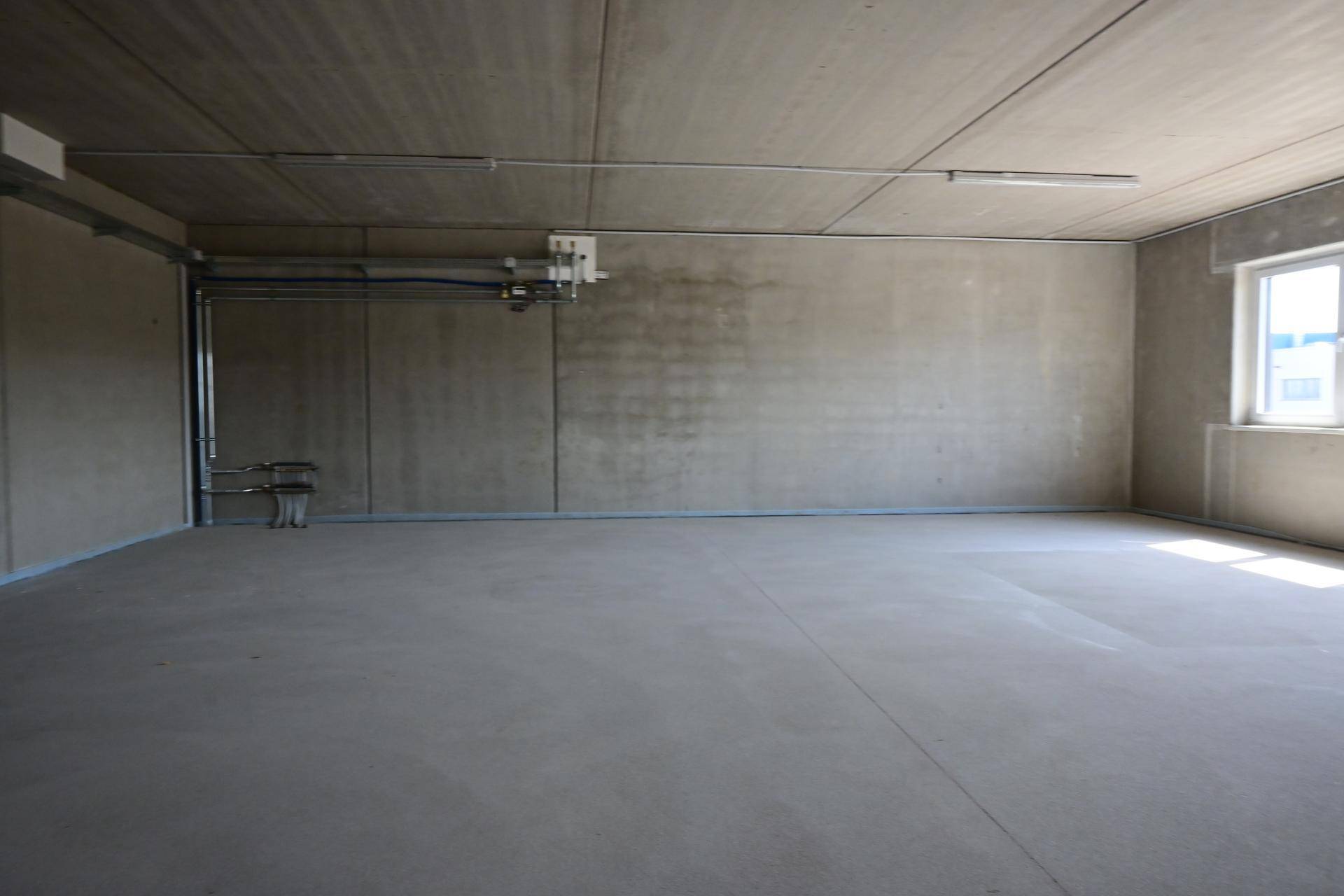 Großer, leerer Gewerberaum mit Betonoberflächen und einem Fenster, das Tageslicht spendet.