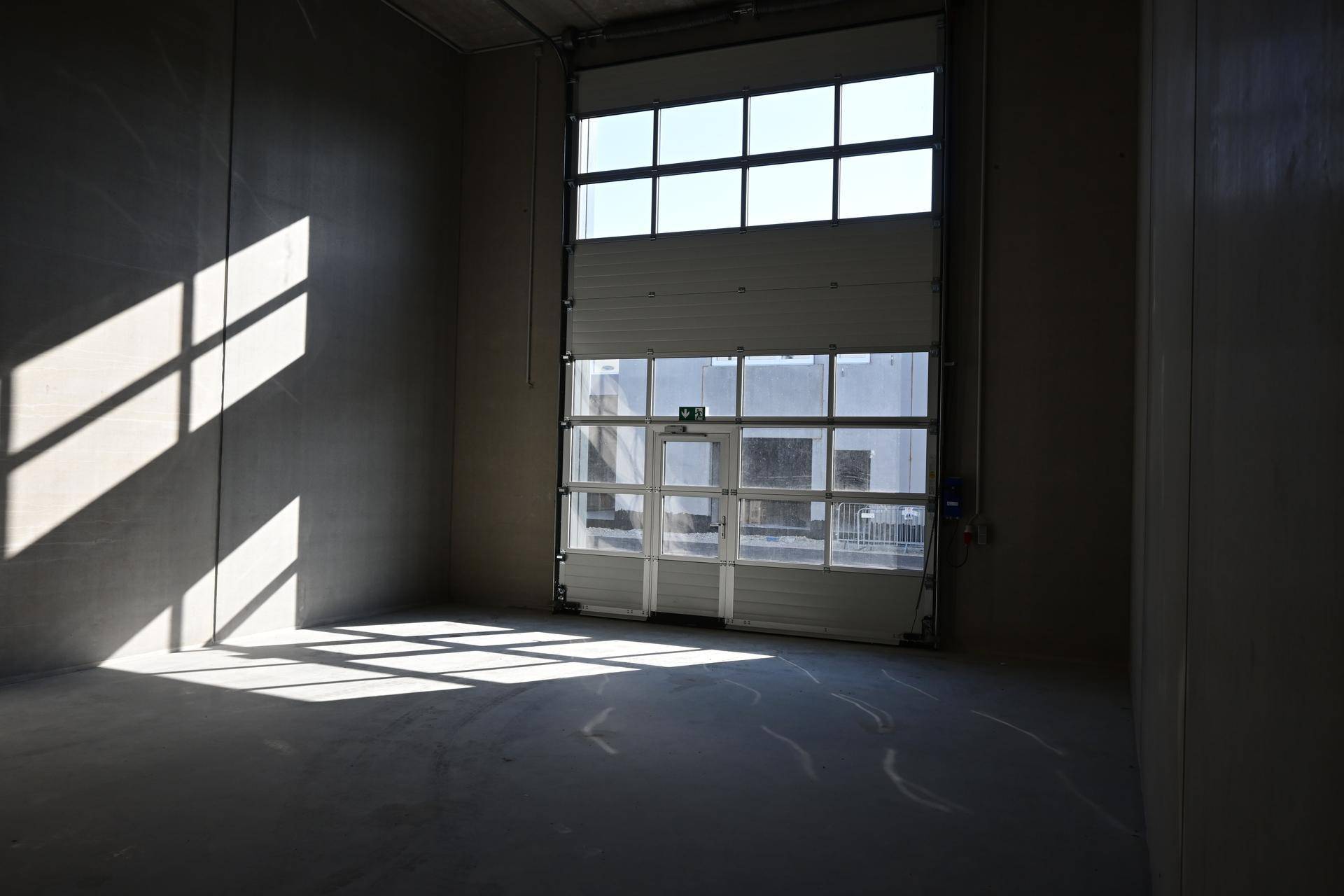 Leere Lagerhalle mit großem Rolltor und viel natürlichem Licht durch die Fenster.
