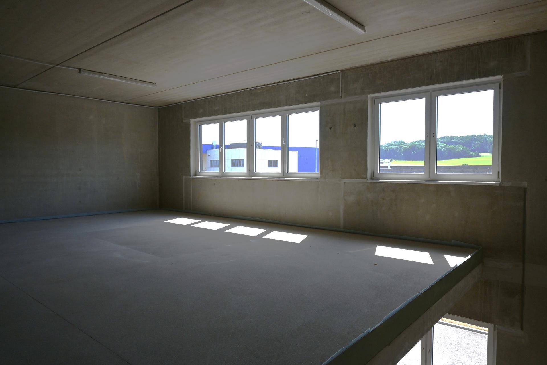 Unfertiger Gewerberaum im Obergeschoss mit Betonboden, hohen Decken und viel Tageslicht durch große Fenster.