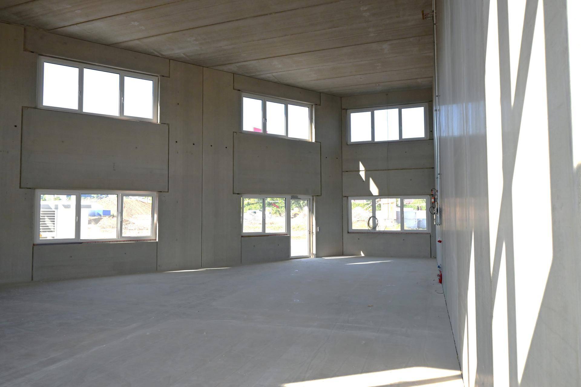 Geräumiger Innenraum mit Betonwänden und vielen Fenstern, ideal für gewerbliche Nutzung.