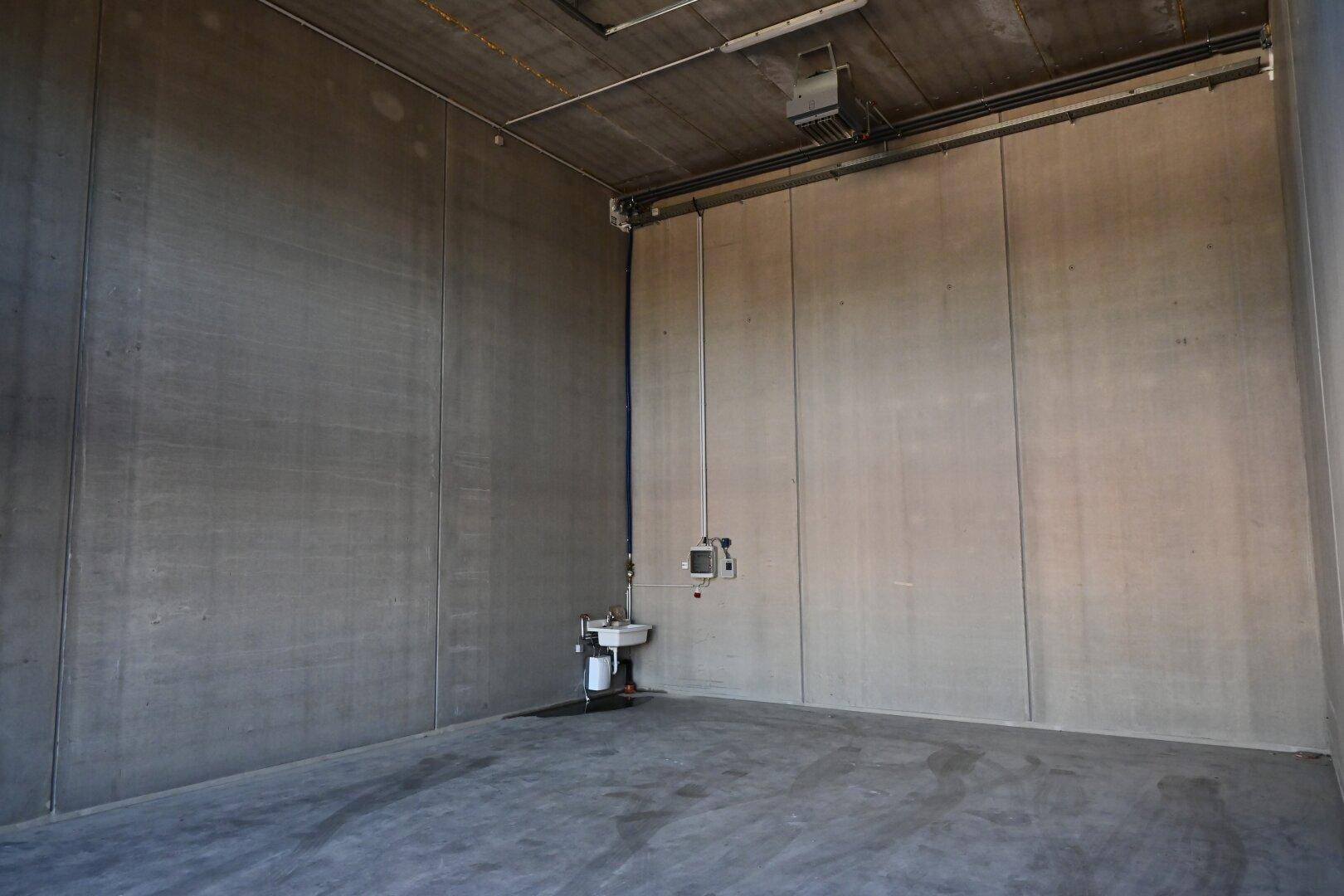 Leerer Industrieraum mit hohen Betonwänden, Betonboden und einem kleinen Waschbecken an der Wand.