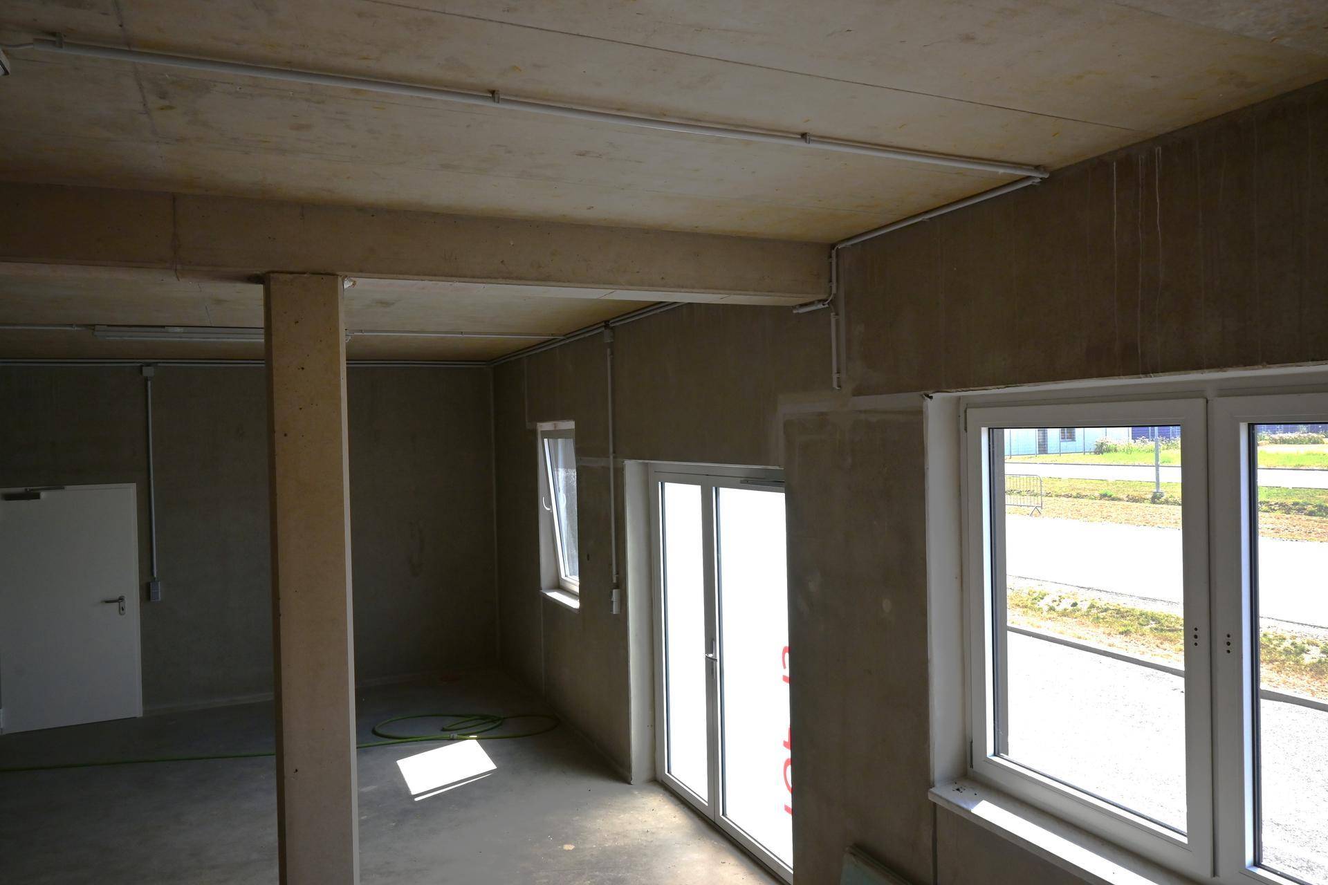 Geräumiger, unfertiger Gewerberaum mit Betonwänden und -boden, der viel natürliches Licht hereinlässt.