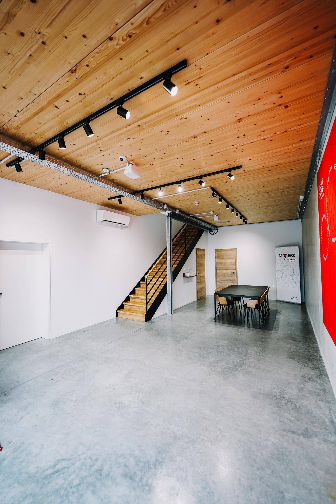 Moderner Gewerberaum mit Holzdecke, Betonboden und Treppe, gut beleuchtet.