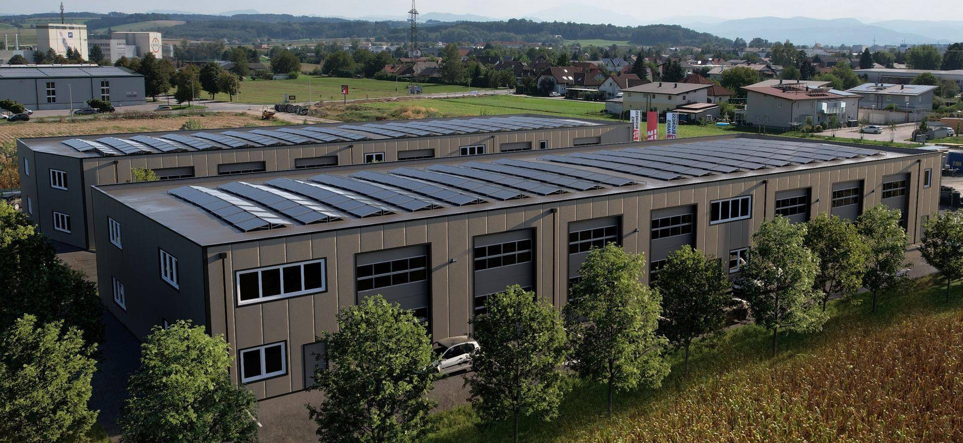 Luftaufnahme eines neuen Gewerbekomplexes mit Solarpaneelen auf dem Dach und angrenzenden Grünflächen.