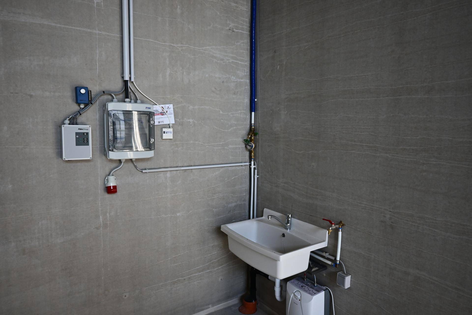 Funktionaler Waschraum mit Waschbecken, Warmwasserbereiter und sichtbaren Installationen an der Wand.