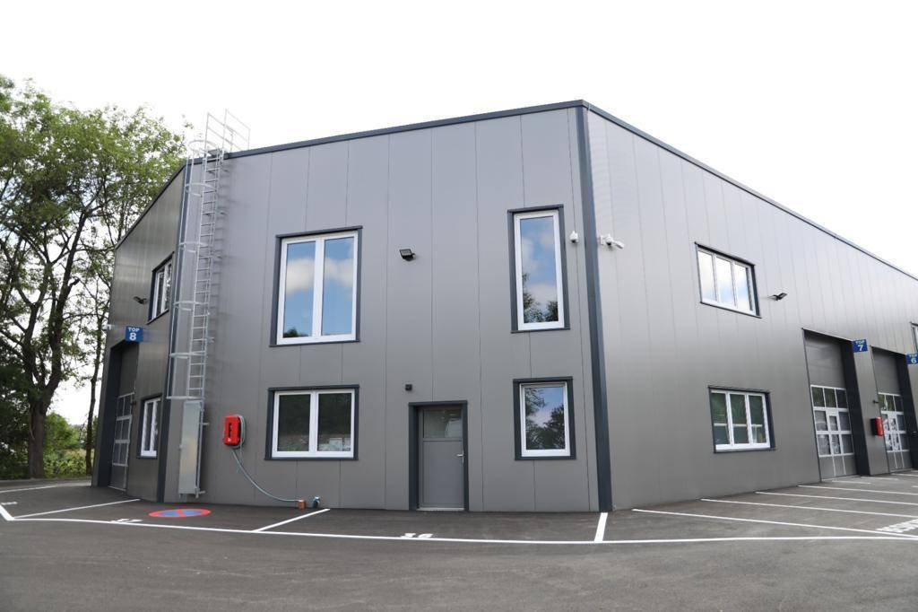 Eckansicht eines modernen Gewerbegebäudes mit grauer Fassade, Fenstern und externer Leiter.