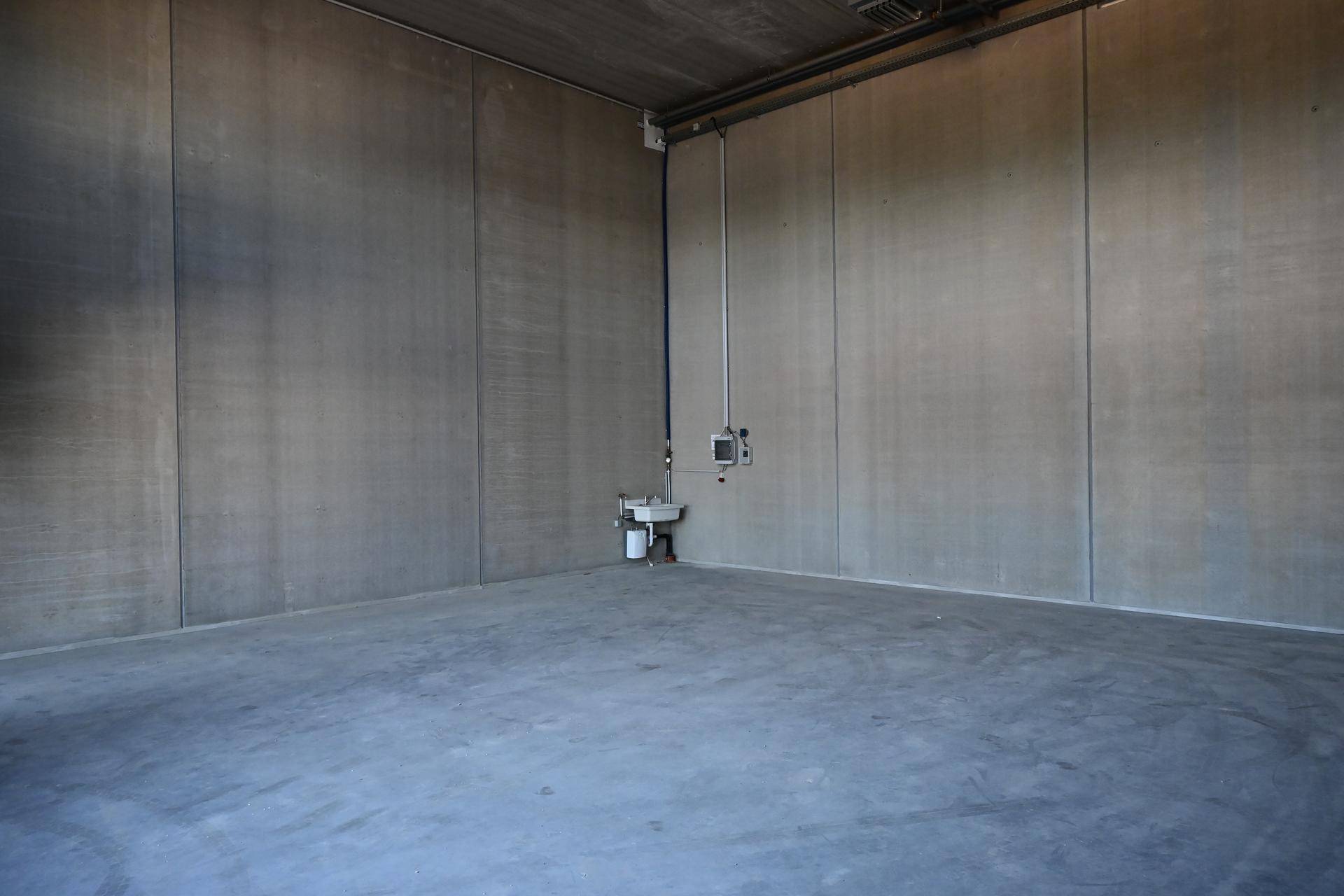Geräumige, leere Lagerhalle mit hohen Decken, Betonwänden und einem Waschbecken.