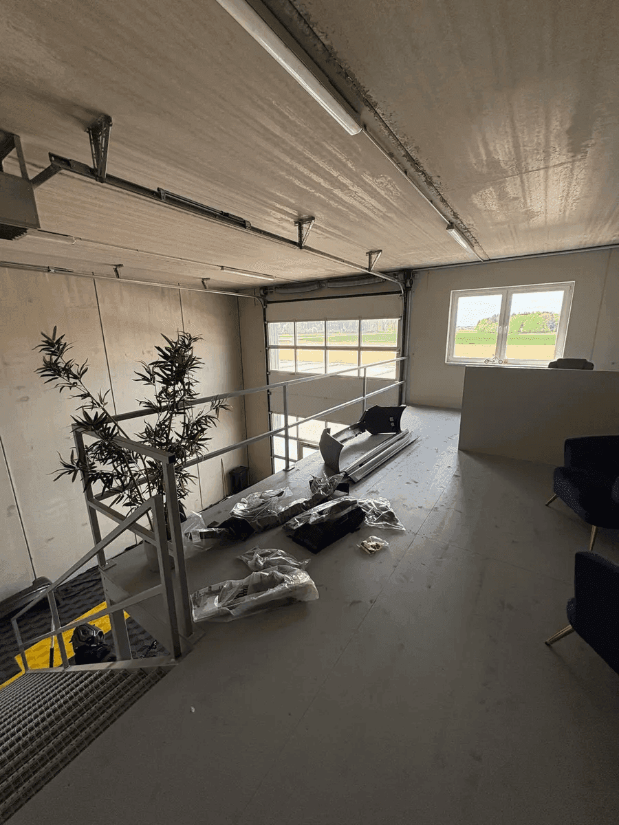 Mezzanine-Ebene einer Werkstatt mit Blick auf ein Rolltor, ein Fenster und eine grüne Landschaft im Hintergrund.