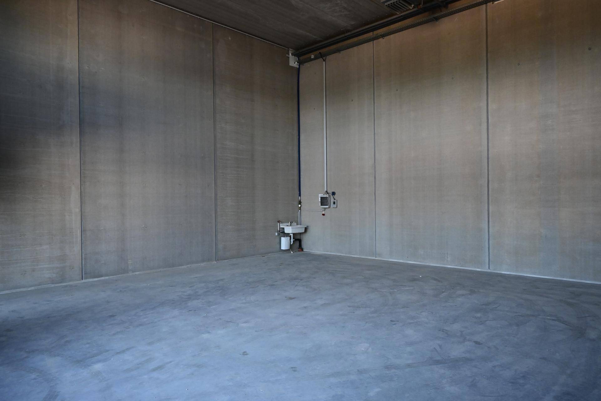 Saubere, leere Lagerhalle mit Betonwänden, Betonboden und einem kleinen Waschbecken an der Wand.